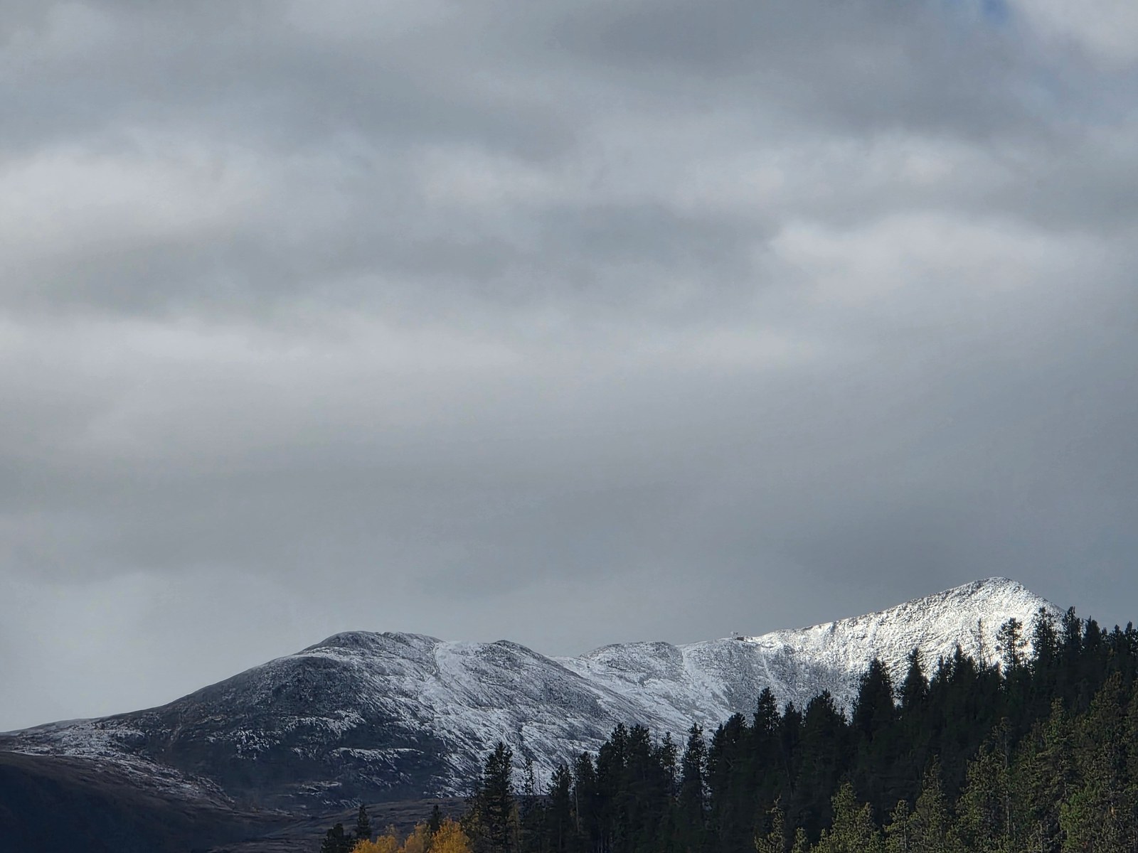 Snow-covered peaks in Summit County under a cloudy October sky